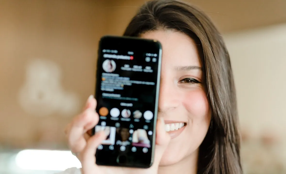Amanda Polastro sorrindo e exibindo o celular com seu Instagram aberto