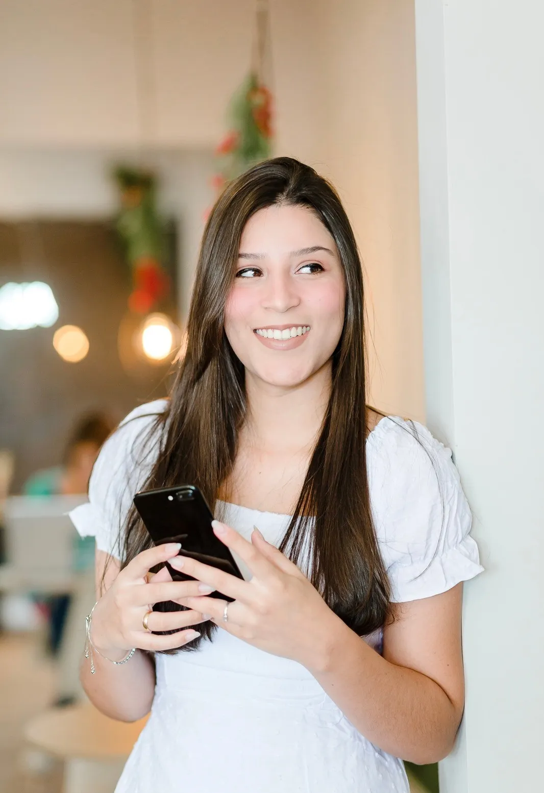 Amanda Polastro em Vestido Branco segurando celular e sorrindo